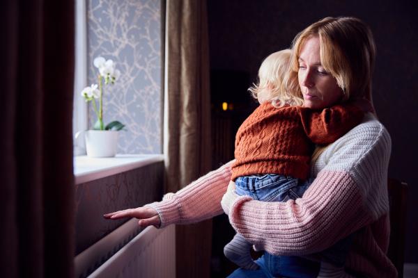 Woman holding a child in warm clothing stood near the radiator